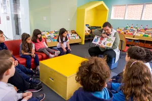 Professora do GDV lendo um livro ilustrado para crianças da Educação Infantil na biblioteca